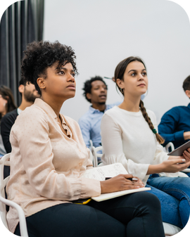 Two women take notes and listen intently to a speaker.